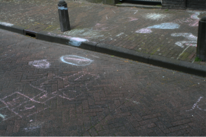 Chalk marks of children's play in public space. Hop scotch etc drawn on to the pavement and road.