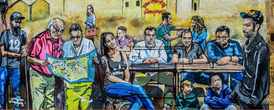 Street art depicting a cafe-like in what could be a town square, people of all ages and backgrounds have come together in a common task. This street art featured on a wall on Pythonos Street in the historic centre of Nicosia, but no longer exists. Credit: Photograph of street art, entitled ‘People of Cyprus’, by street artist Paparazzi.